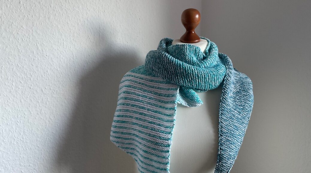 Querkant-Fotos. Blau-weiß meliertes gestricktes Tuch. Hängt - wie immer - über die Schultern meiner Schneiderpuppe. Vor der berühmten weißen Wand, die gerade etwas schattig-grau ist. Links über der Schulter ist der Schal blau-weiß gestreift, der Rest des Schals ist hellblau-weiß meliert. Im oberen rechten Bereich des Bildes ist der Text "Handmade by © AnneluM" zu sehen.